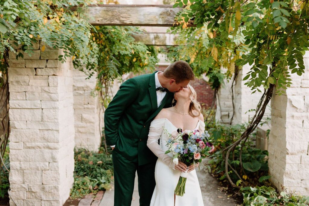 Bride and groom kissing under pergola at Lauritzen Gardens wedding.