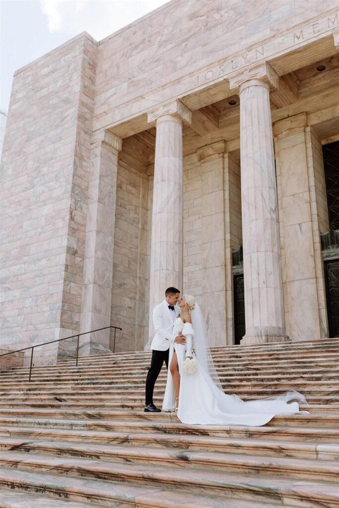 Newlyweds pose on front staircase of The Joslyn Art Museum in Omaha NE.